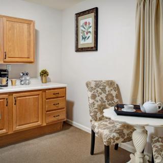 A cozy kitchen nook with wooden cabinets, a small round table set for tea, and decorative curtains.