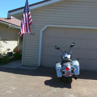 A motorcycle parked in front of a house, with an American flag proudly displayed.