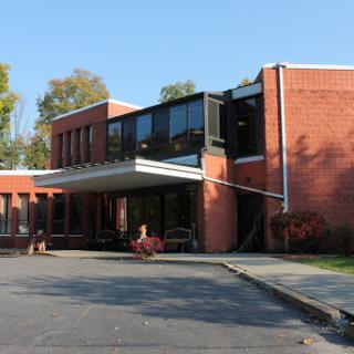 A modern brick building featuring large windows and a welcoming entrance surrounded by trees.