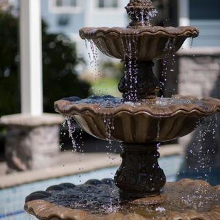 A multi-tiered garden fountain with water cascading from the top basin.
