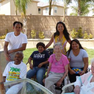 A diverse group of people poses together for a photo outdoors, enjoying a sunny day in a backyard setting.
