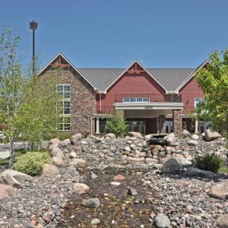 A building with a stone facade surrounded by landscaped rocks and a small stream under a clear blue sky.