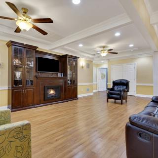 A spacious living room with hardwood floors, featuring a fireplace, built-in entertainment center, and ceiling fans.