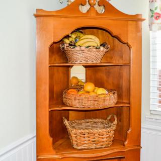 A wooden corner cabinet with baskets containing various fruits.