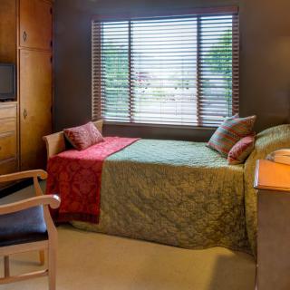 A cozy bedroom with a single bed, colorful quilt, and window with blinds.