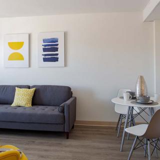 A modern living room with a gray sofa, colorful artwork, and a small dining area.