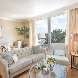 A bright and airy living room with modern decor, featuring a comfortable sofa, an armchair, a glass coffee table, and large windows allowing plenty of natural light.