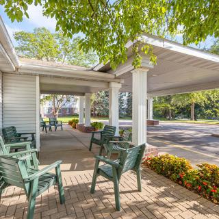 A peaceful outdoor seating area with green chairs under a canopy, surrounded by trees on a sunny day.