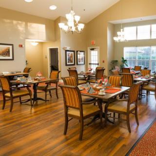 A well-lit dining area with neatly arranged tables and chairs, featuring elegant chandeliers and wooden flooring.