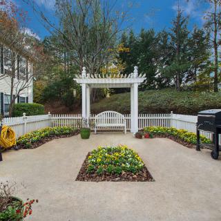 A serene garden with a white bench under a pergola, surrounded by colorful flowers and greenery.