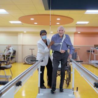 A healthcare professional assists an elderly patient during a physical therapy session, focusing on walking and rehabilitation.