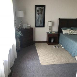 A cozy bedroom with a neatly made bed, nightstands, and lamps, complemented by a soft carpet and decorative elements.