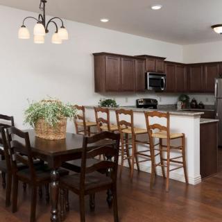 A modern kitchen and dining area featuring wooden cabinets, a large dining table, and bar stools lined up along the counter.