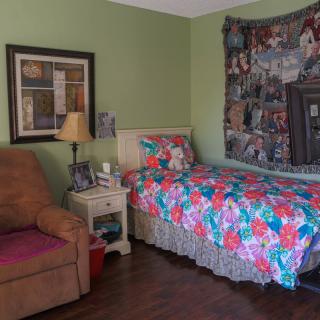 A cozy bedroom featuring a single bed with a colorful quilt, an armchair, and various wall decorations.