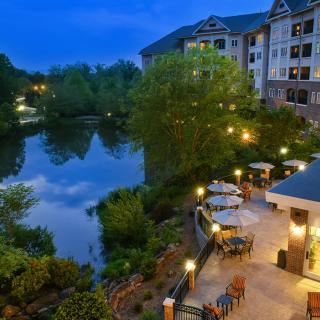 A scenic view of a hotel by the river during the evening, featuring outdoor seating and illuminated surroundings.