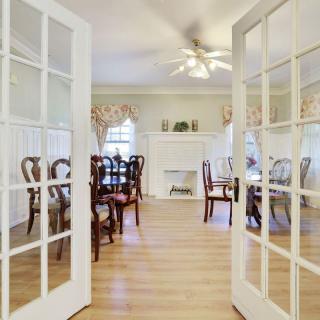 A spacious dining room with elegant furniture, featuring French doors and a classic fireplace.