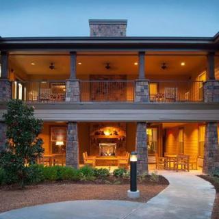 A warmly lit two-story house with a porch and pathway leading to the entrance at dusk.