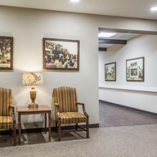A lobby area with striped chairs, a lamp, and framed artwork leading to a hallway.