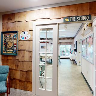 Entrance to an art studio with glass doors and wooden walls, inviting creativity.