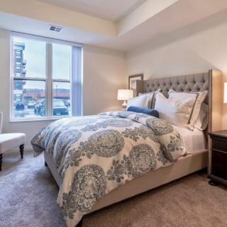 A cozy and well-decorated bedroom featuring a plush bed with patterned bedding, two lamps on nightstands, and a large window providing natural light.