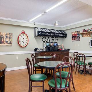 A cozy cafe interior featuring round tables, chairs with green cushions, a coffee station, and vintage decor.