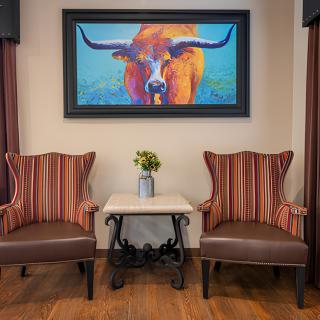 A cozy interior with two striped chairs, a small table, and a vibrant longhorn painting on the wall.