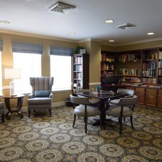 A cozy library room with bookshelves, a table, and comfortable chairs for reading.