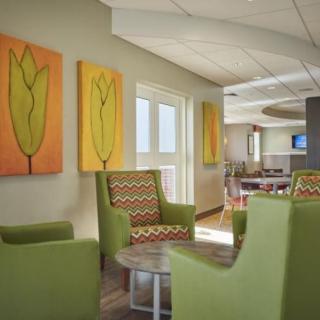 A modern lounge area with green chairs and abstract floral paintings on the walls.