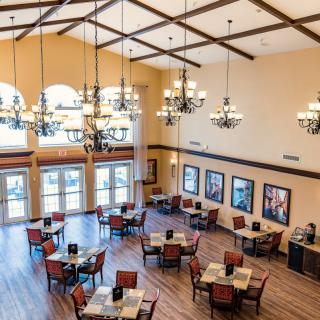A spacious dining area with elegant chandeliers, wooden flooring, and neatly arranged tables and chairs.