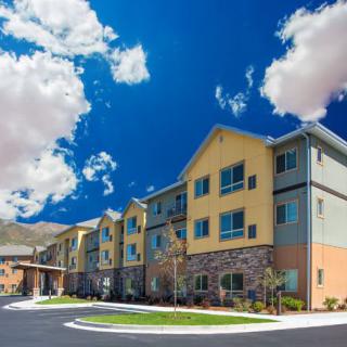 A modern residential apartment complex under a bright blue sky with fluffy clouds.
