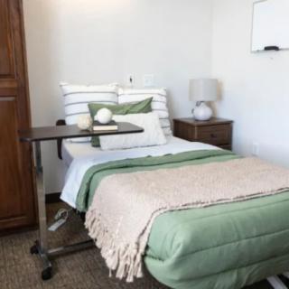 A neatly arranged hospital room with a bed, bedside table, and medical overbed table.