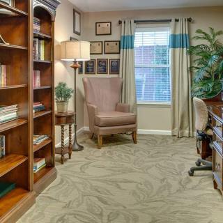 A cozy home office with bookshelves, an armchair, and a desk by the window.