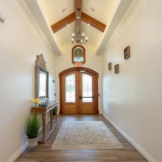 A well-lit hallway with a chandelier, mirror, and decorative elements leading to a wooden double door.