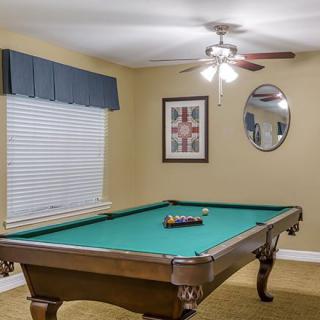 A cozy game room with a pool table, adorned with framed artwork and a ceiling fan.