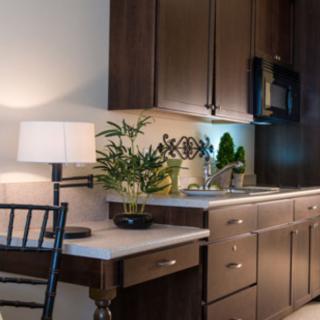 A modern kitchen with dark wood cabinets and a small desk area, featuring a lamp and green plant for decoration.