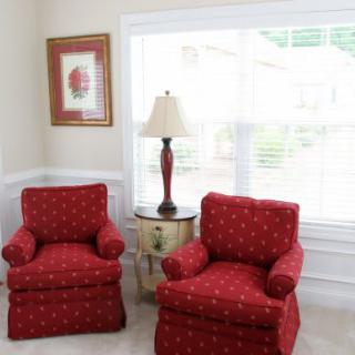 A cozy living room corner with two red armchairs, a lamp, and a side table by the window.