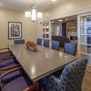A stylish dining room with a large conference table surrounded by patterned chairs, featuring elegant lighting and wall artwork.