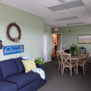 A cozy living room with a blue sofa and a round dining table, featuring decorative elements like a wreath and a sign.