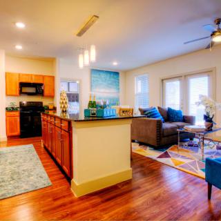 A modern open-layout living room and kitchen with hardwood floors and colorful decor.