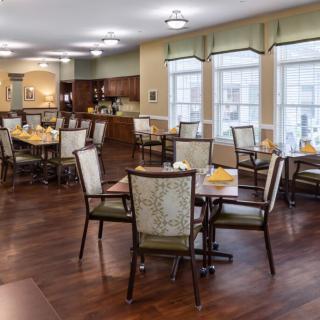 A spacious dining area with neatly arranged tables and chairs on a wooden floor.