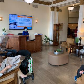 A modern lobby with people seated, a reception desk, and a television displaying information.
