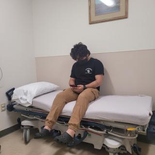 A patient sitting on a hospital bed, absorbed in their phone while waiting for medical attention.
