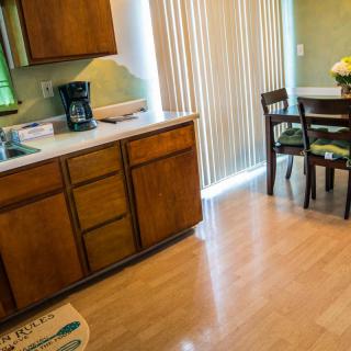 A cozy kitchen and dining area featuring wooden cabinets, a coffee maker, and a small round table with chairs near a sliding door.