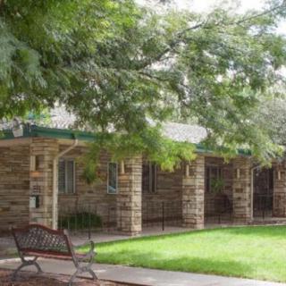 A stone building with a green lawn and a bench under the shade of trees.