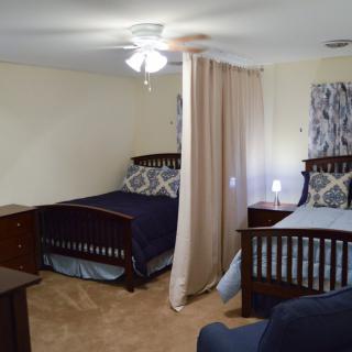 A bedroom with two beds separated by a curtain, featuring a ceiling fan and simple decor.