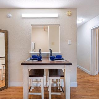 A cozy dining area features a table set for two with blue dishware, positioned next to a kitchen pass-through and adorned with wooden flooring.