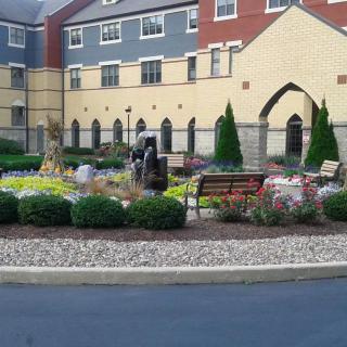 A landscaped garden with colorful flowers and a bench in front of a multi-story building.