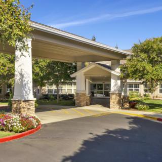 A building entrance with a covered driveway, surrounded by trees and well-maintained landscaping.
