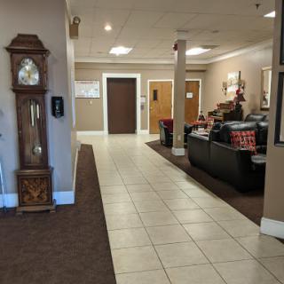 A spacious and welcoming lobby featuring a classic clock, comfortable seating, and an elevator.