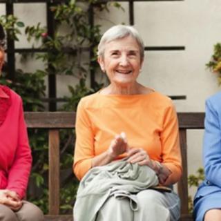 Three elderly women sitting on a bench outdoors, smiling and enjoying their time together.